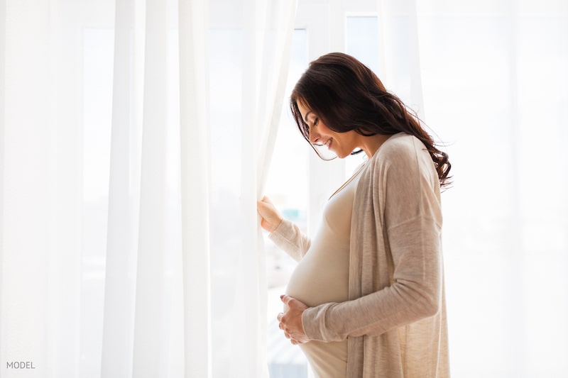 Pregnant woman holding her stomach in front of a white background.