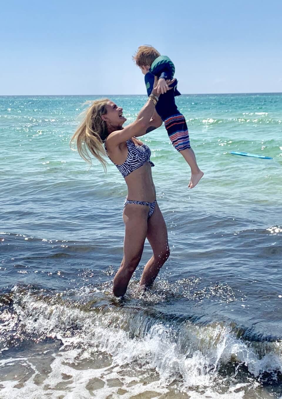 Kelly with her son at the beach. Kelly is lifting her kid up in the air.